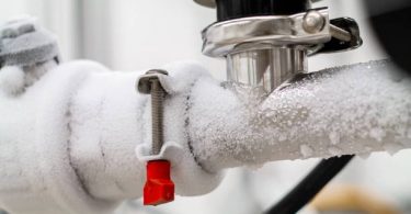 Frozen liquid nitrogen carrying pipes with a valve and black plastic lever close up in a science laboratory 2020